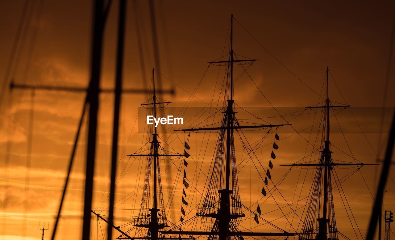 Sailboats moored on harbor against sky during sunset