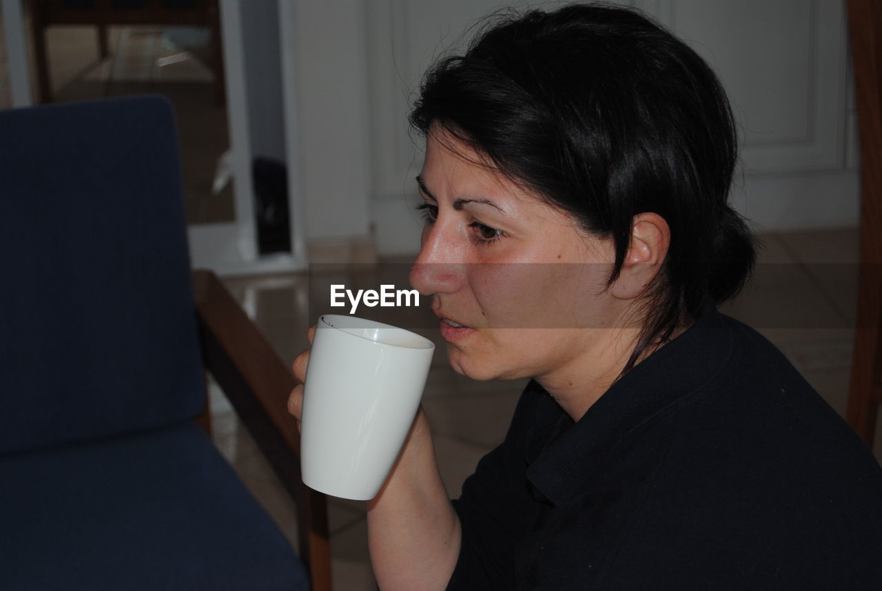 Side view of thoughtful woman with mug sitting at home