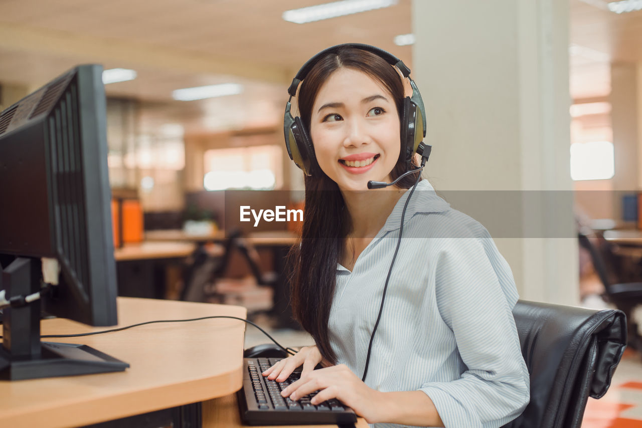 Smiling customer service representative talking on headset while working in office