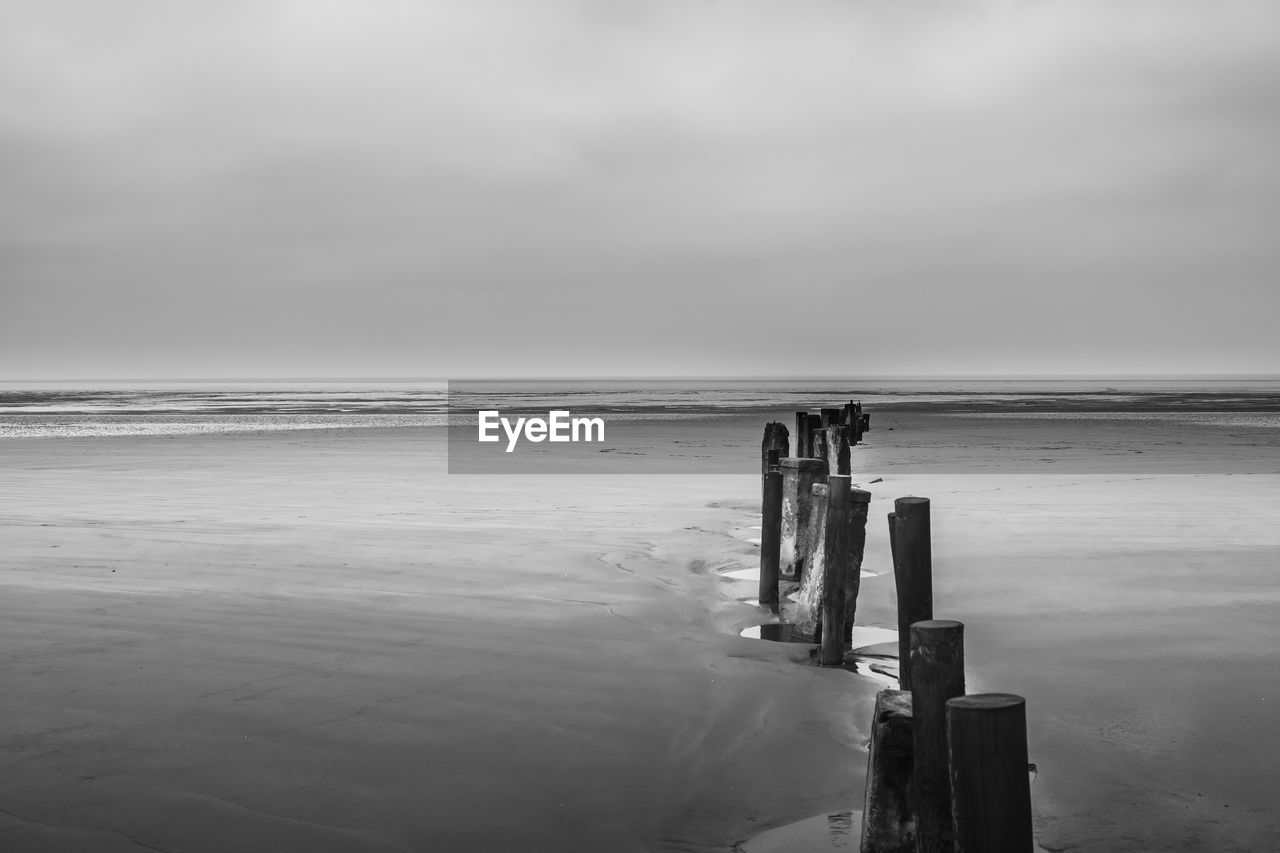 Wooden posts at beach against sky