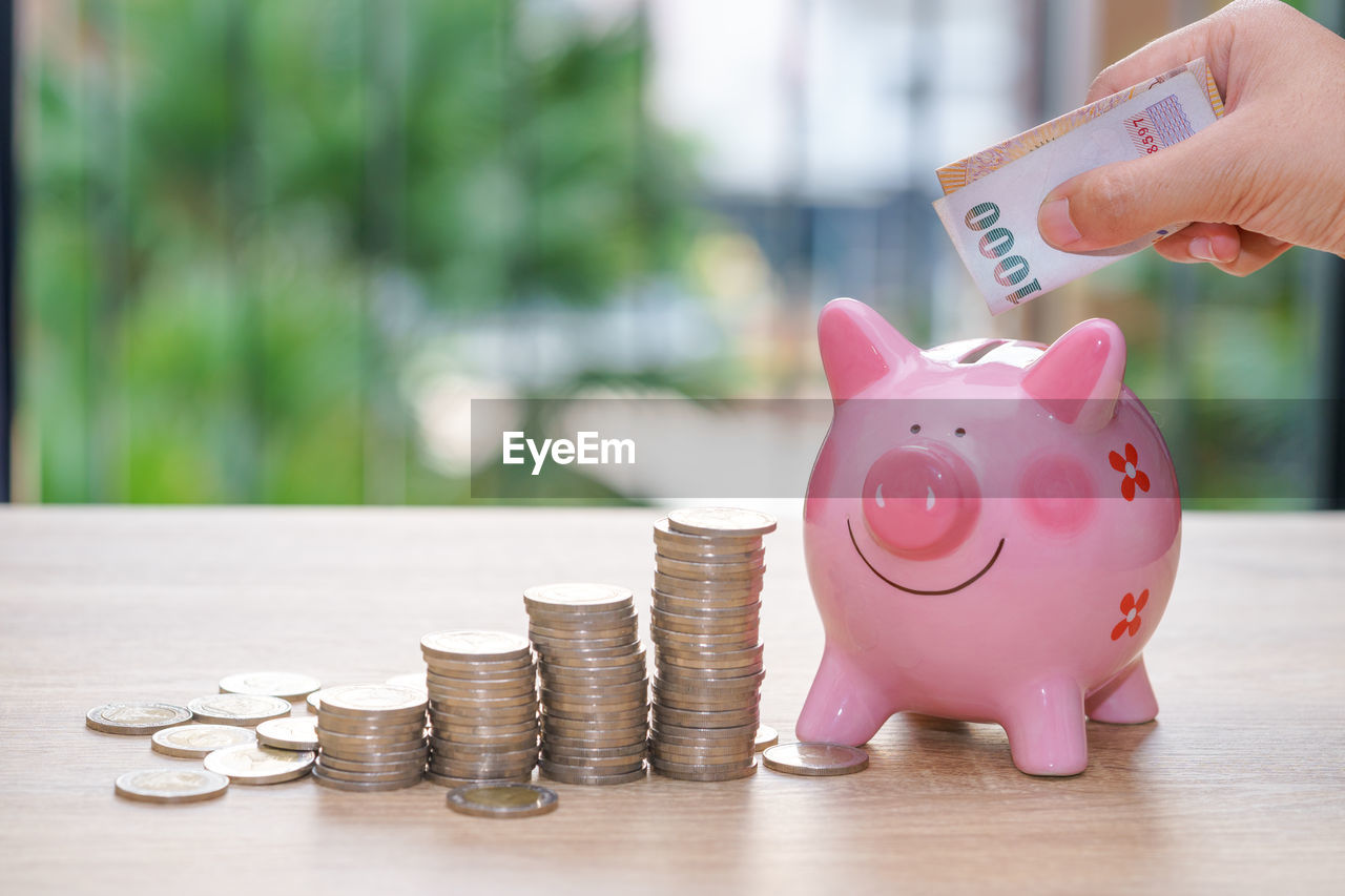 Midsection of woman putting coin in piggy bank at table