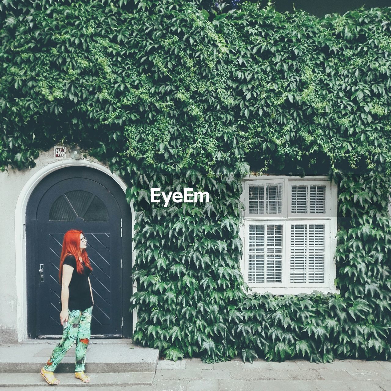 Full length of woman standing against house covered with ivy leaves