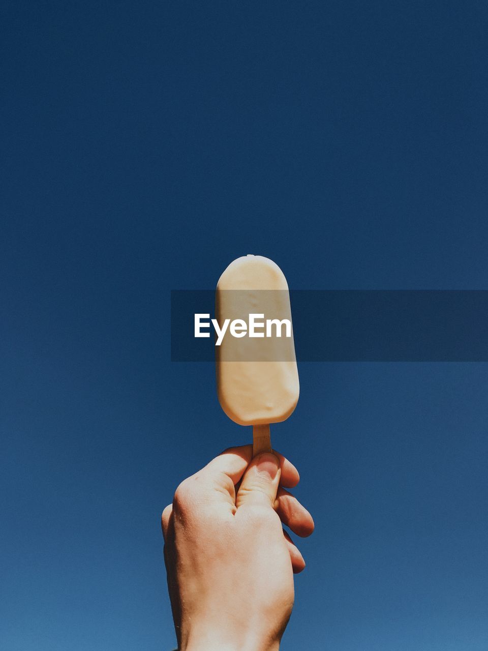 Close-up of hand holding ice cream against blue sky
