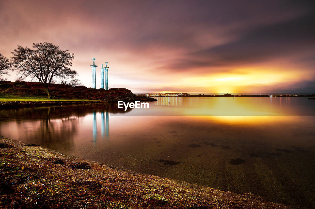 water, reflection, sky, morning, cloud, dawn, nature, sunrise, beauty in nature, sea, scenics - nature, horizon, beach, tranquility, environment, land, architecture, sunlight, tranquil scene, landscape, tree, no people, built structure, outdoors, travel destinations, lighthouse, plant, dramatic sky, shore, idyllic, building, building exterior, travel