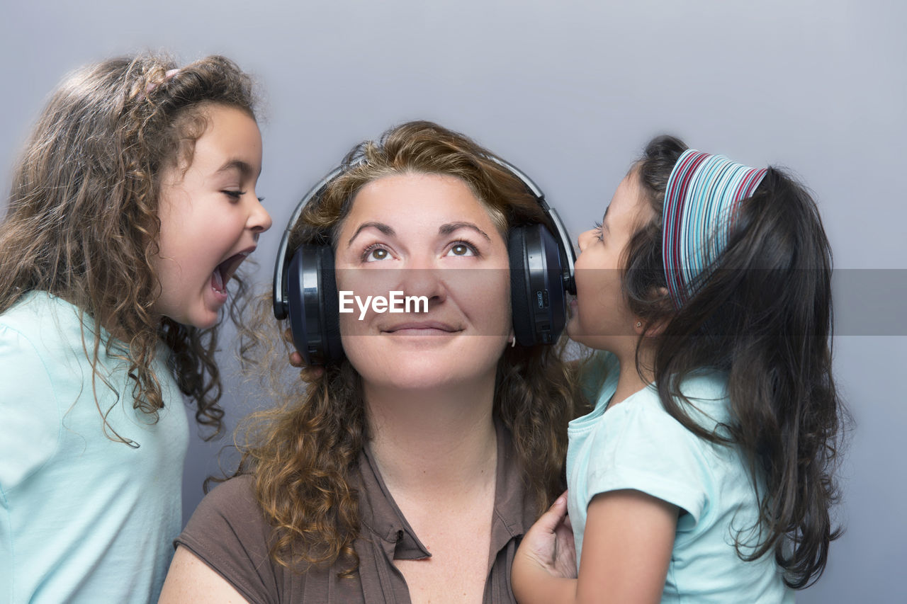 Daughters shouting amidst mother wearing headphones by wall