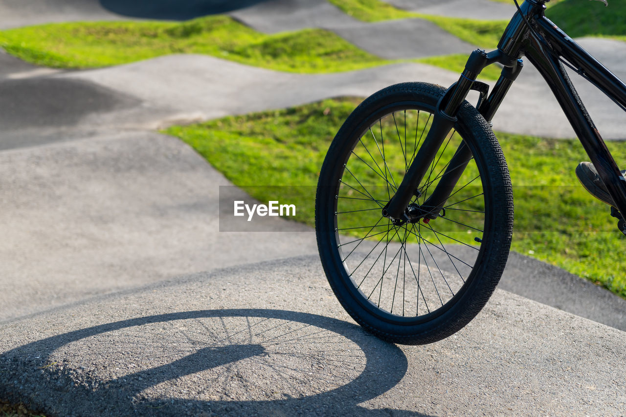 Bicycle wheel on asphalt pump track surrounded by grass and nature on a sunny day. 