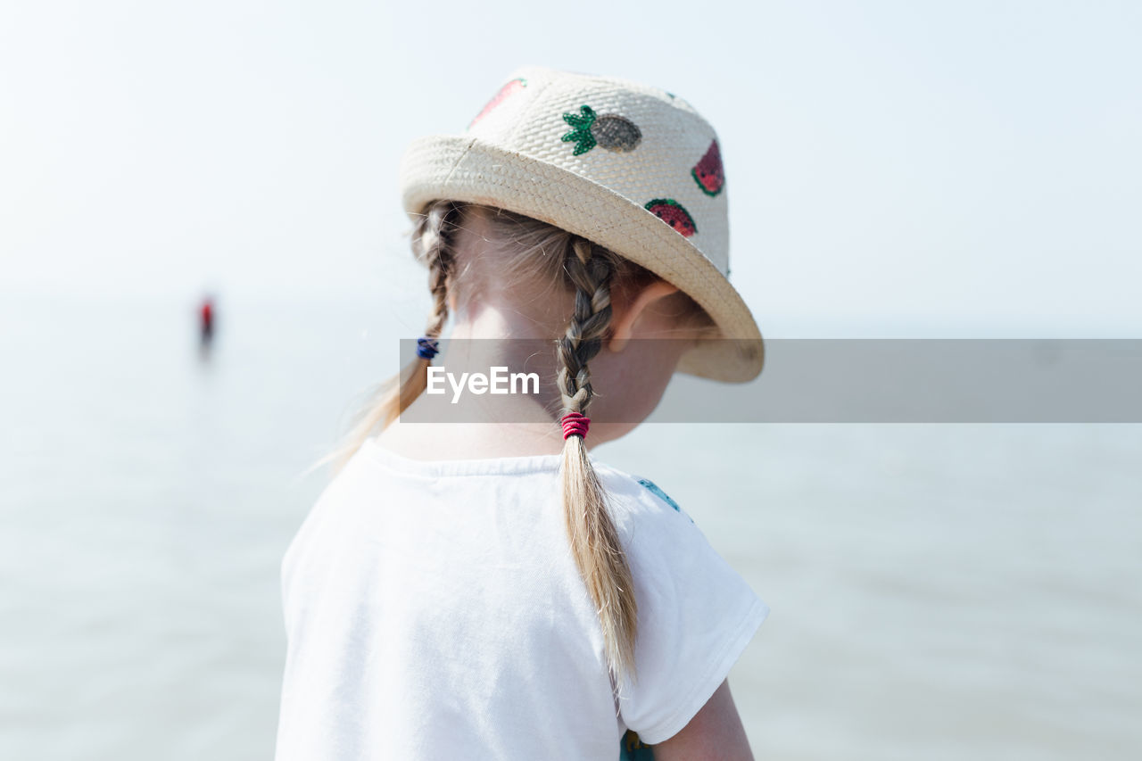 Girl wearing hat standing by sea against sky during sunny day