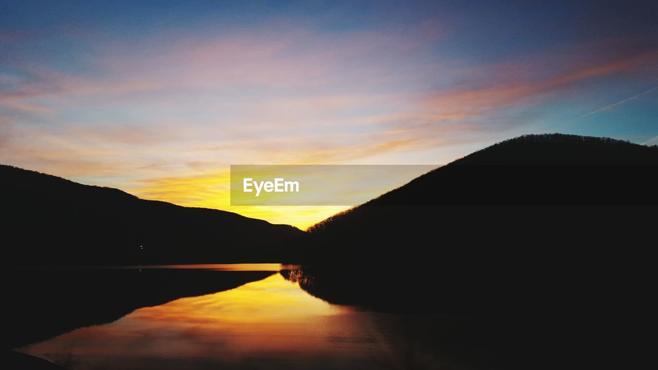 Scenic view of river and silhouette mountains at sunset