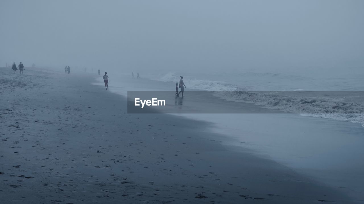 People at beach during fogy weather against sky
