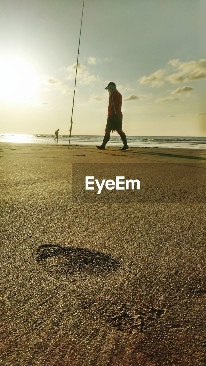 Full length of man walking on sand at beach against sky during sunset