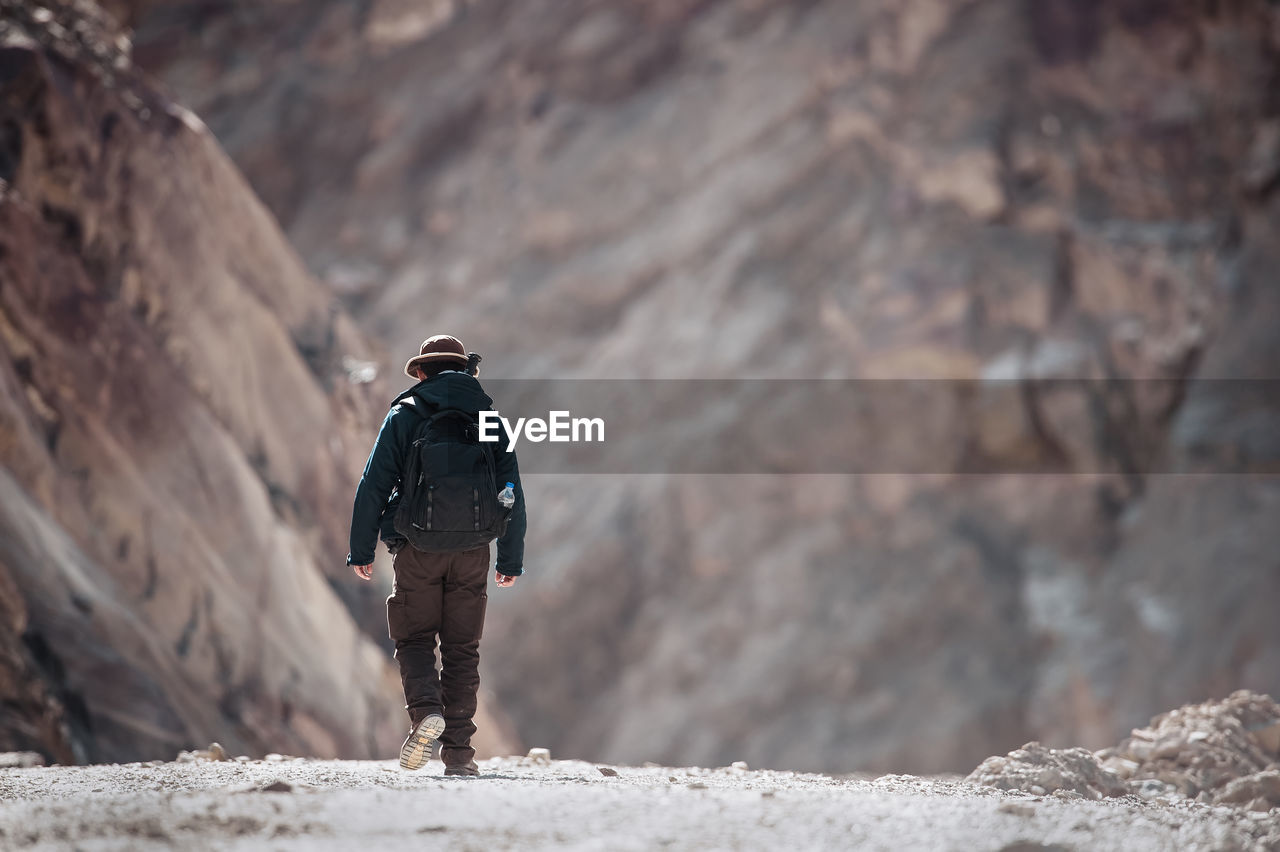 REAR VIEW OF MAN STANDING ON ROCK AGAINST MOUNTAINS