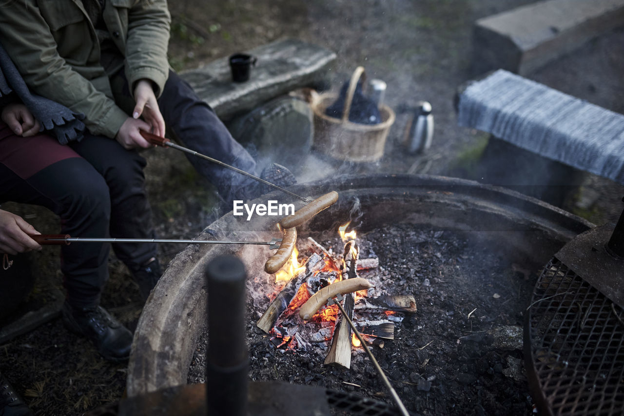 People preparing hotdogs over campfire