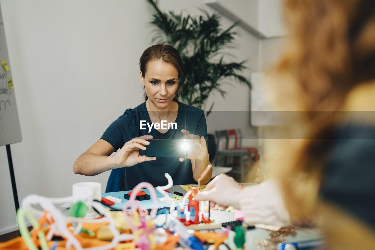 Confident businesswoman photographing stationery on table at creative office