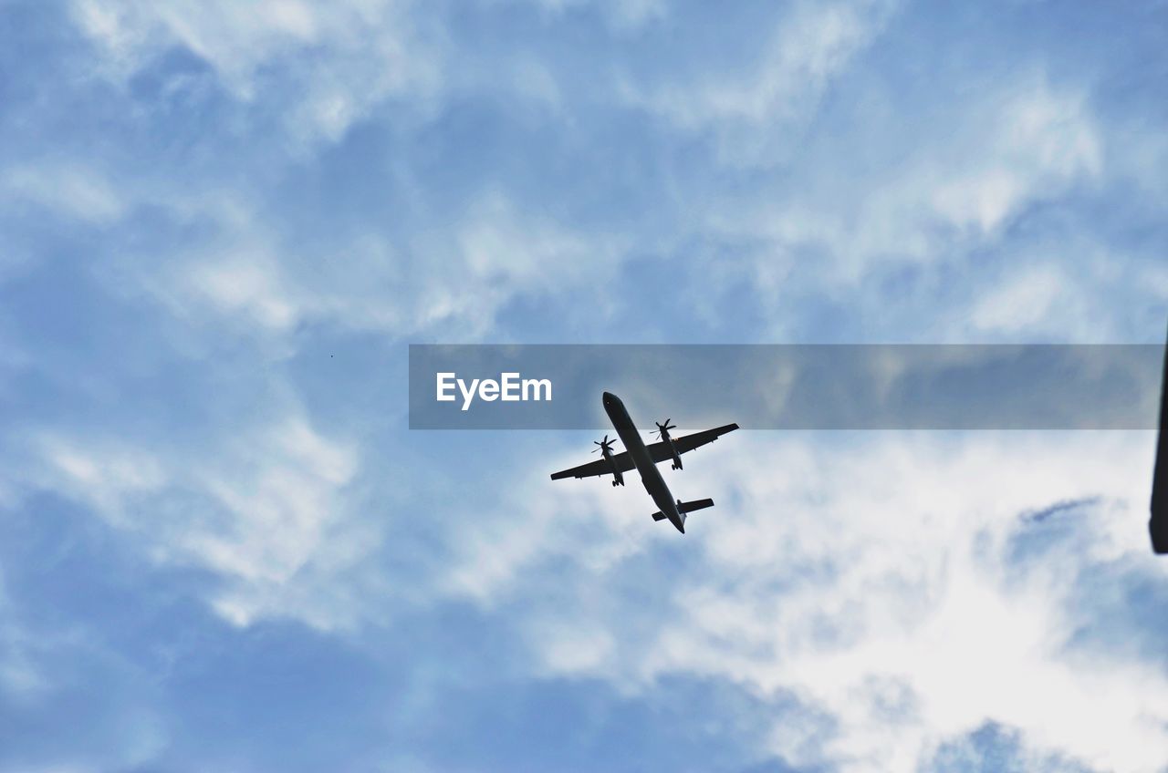 Low angle view of airplane flying against cloudy sky