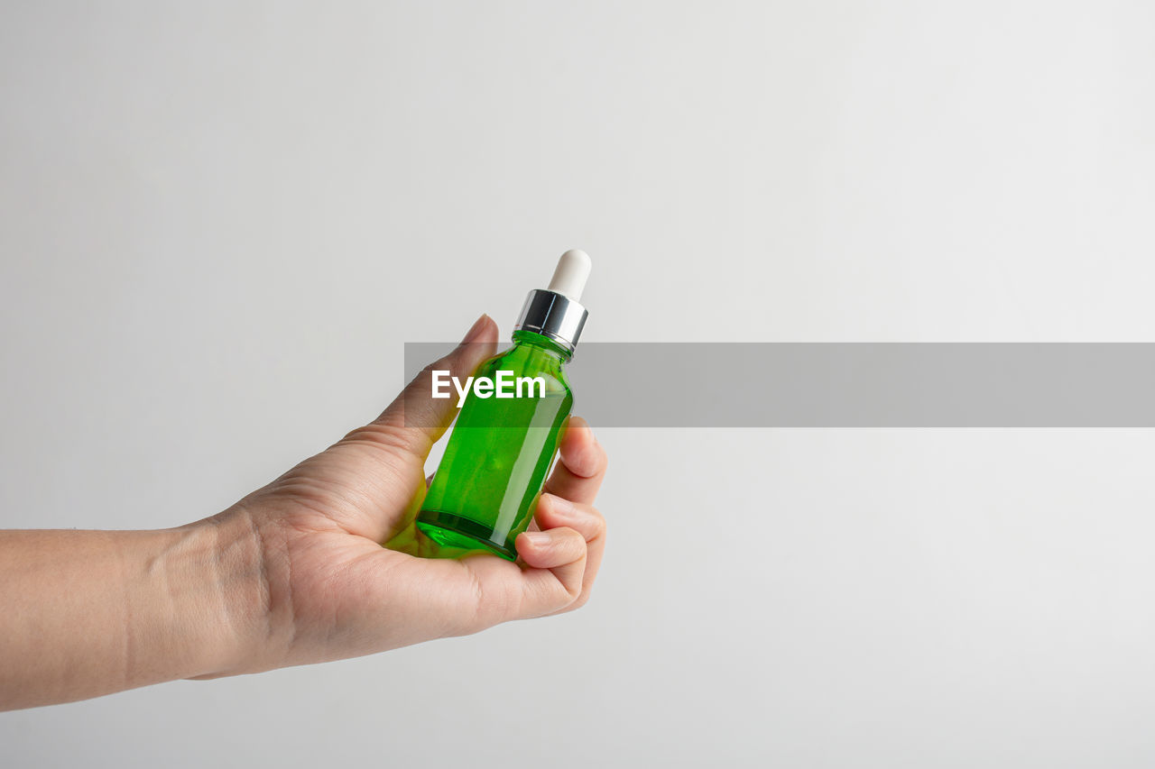 Hand holding up a green glass dropper bottle on white background