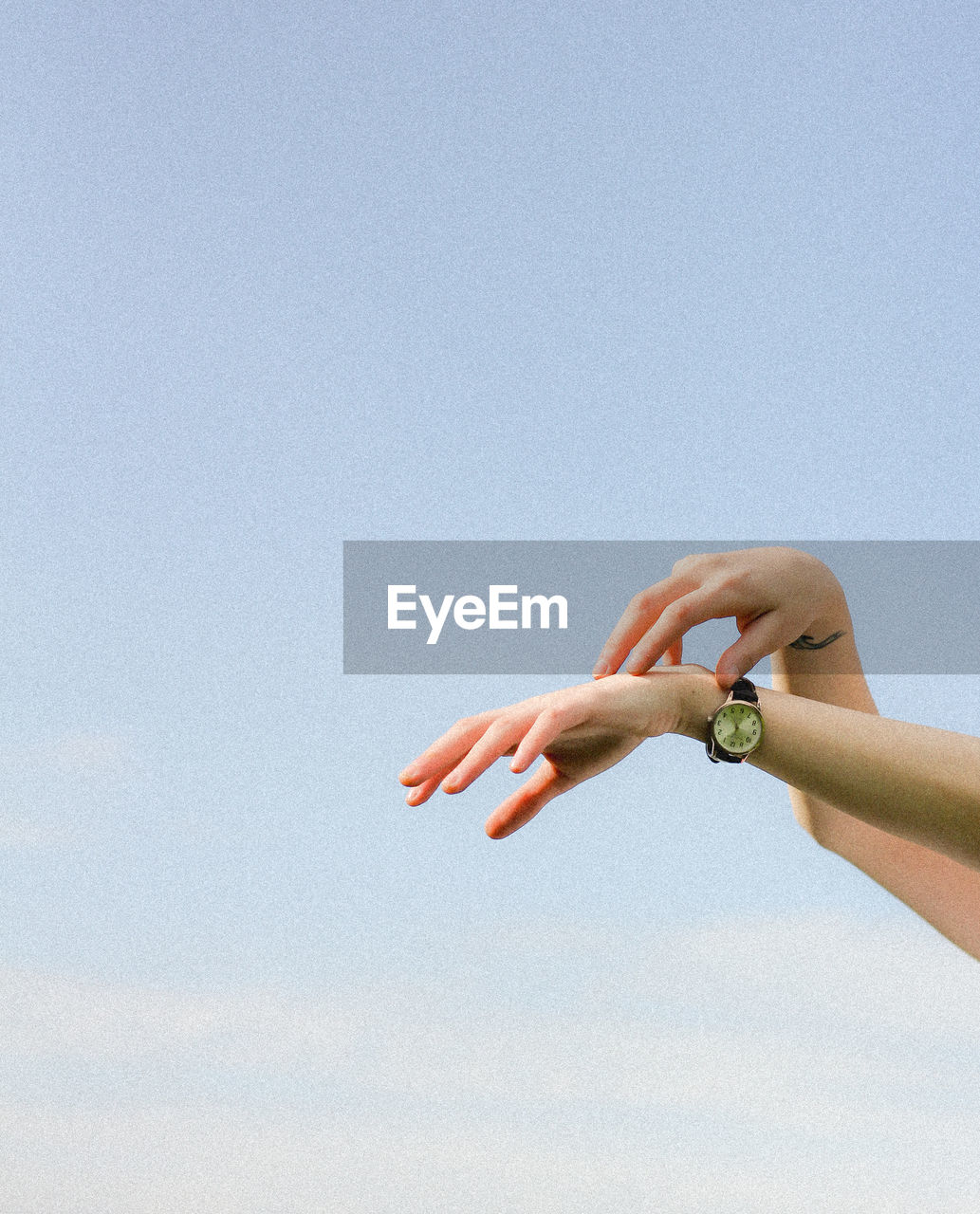 Cropped hands of woman wearing wristwatch against clear sky