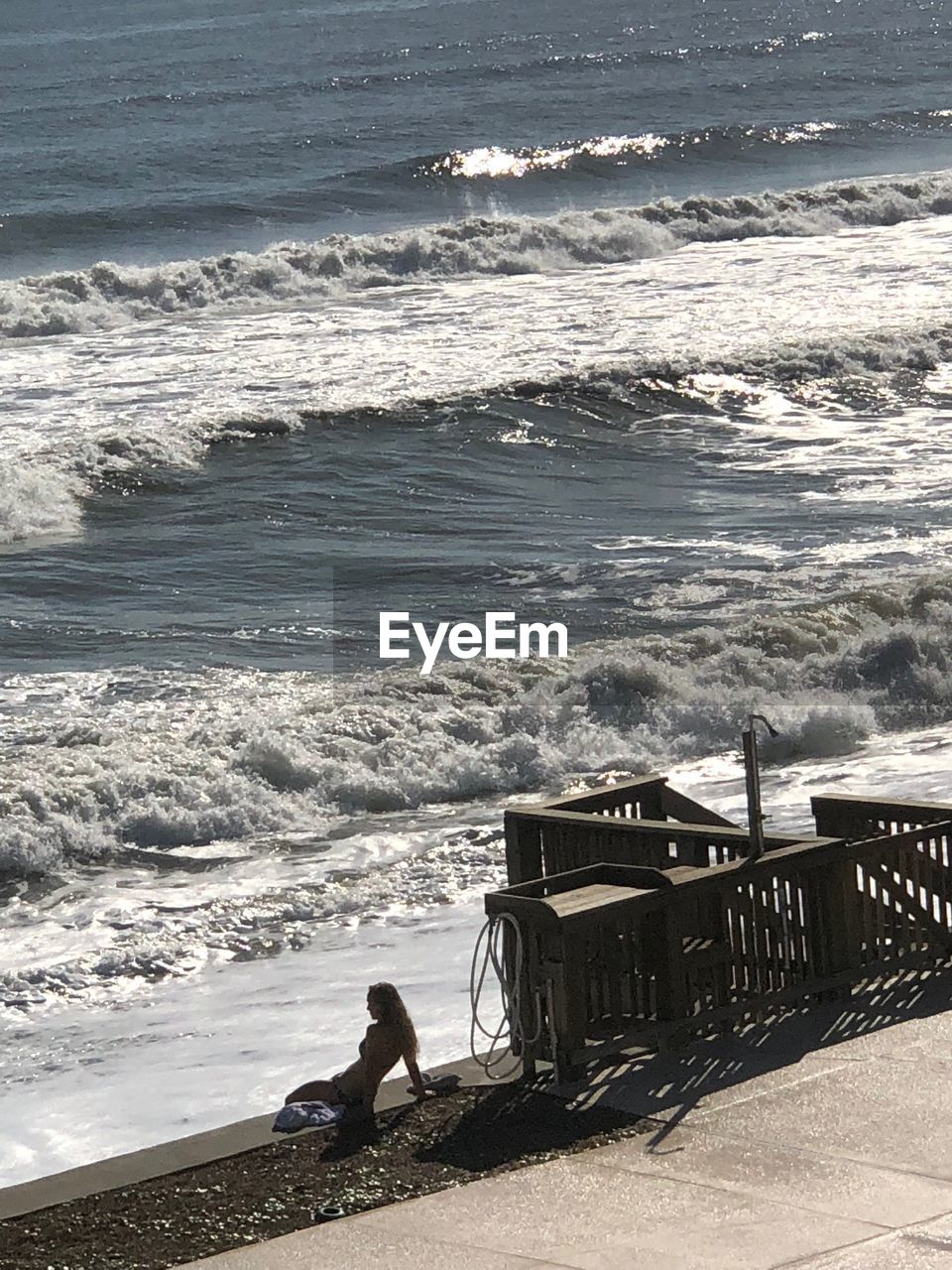 MAN SITTING ON BEACH AGAINST SEA