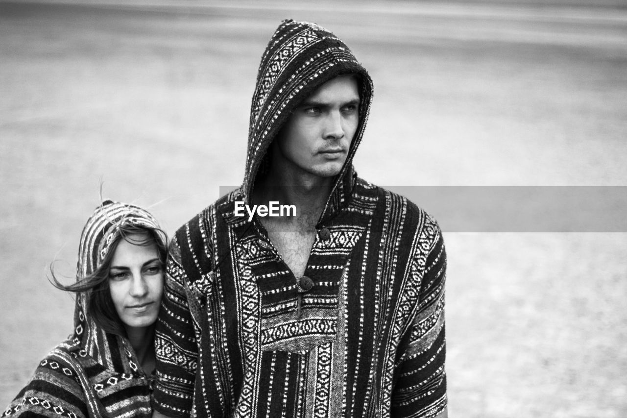 Couple in hooded clothing looking away while standing on field