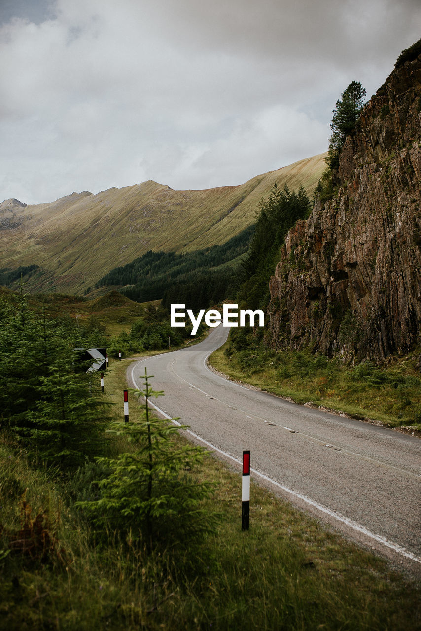 Empty road by mountains against cloudy sky