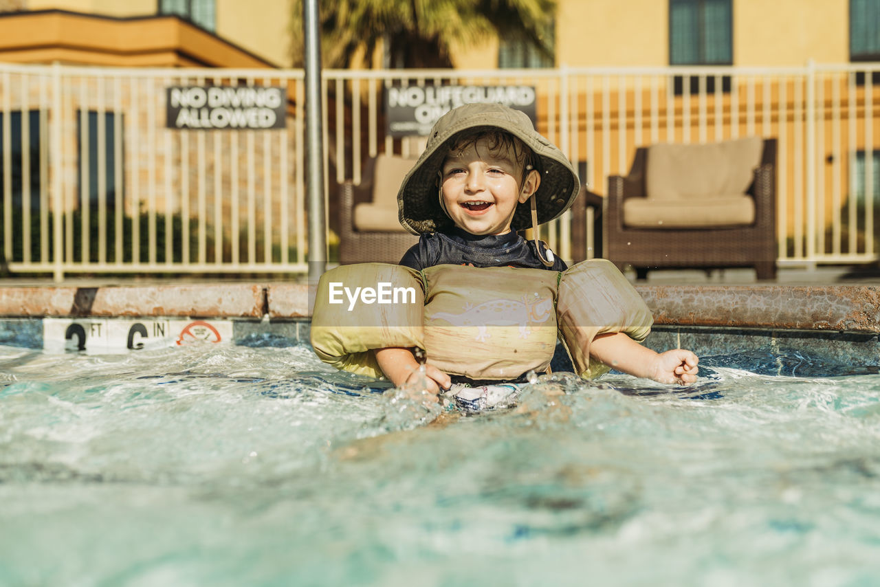 Front view of young toddler boy sitting in hotel pool on vacation