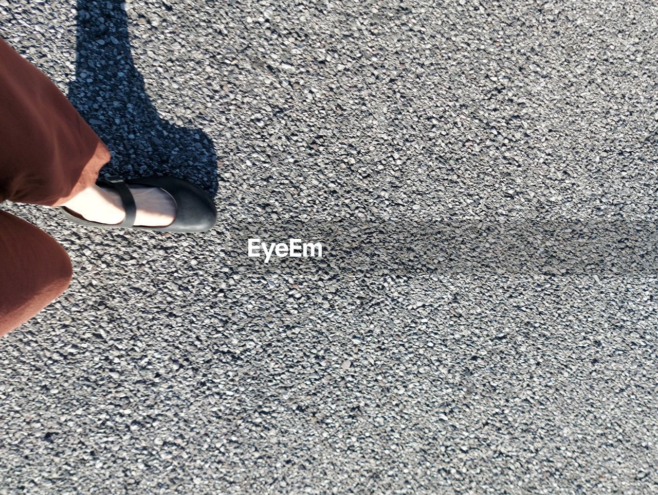 LOW SECTION OF WOMAN STANDING ON ASPHALT ROAD