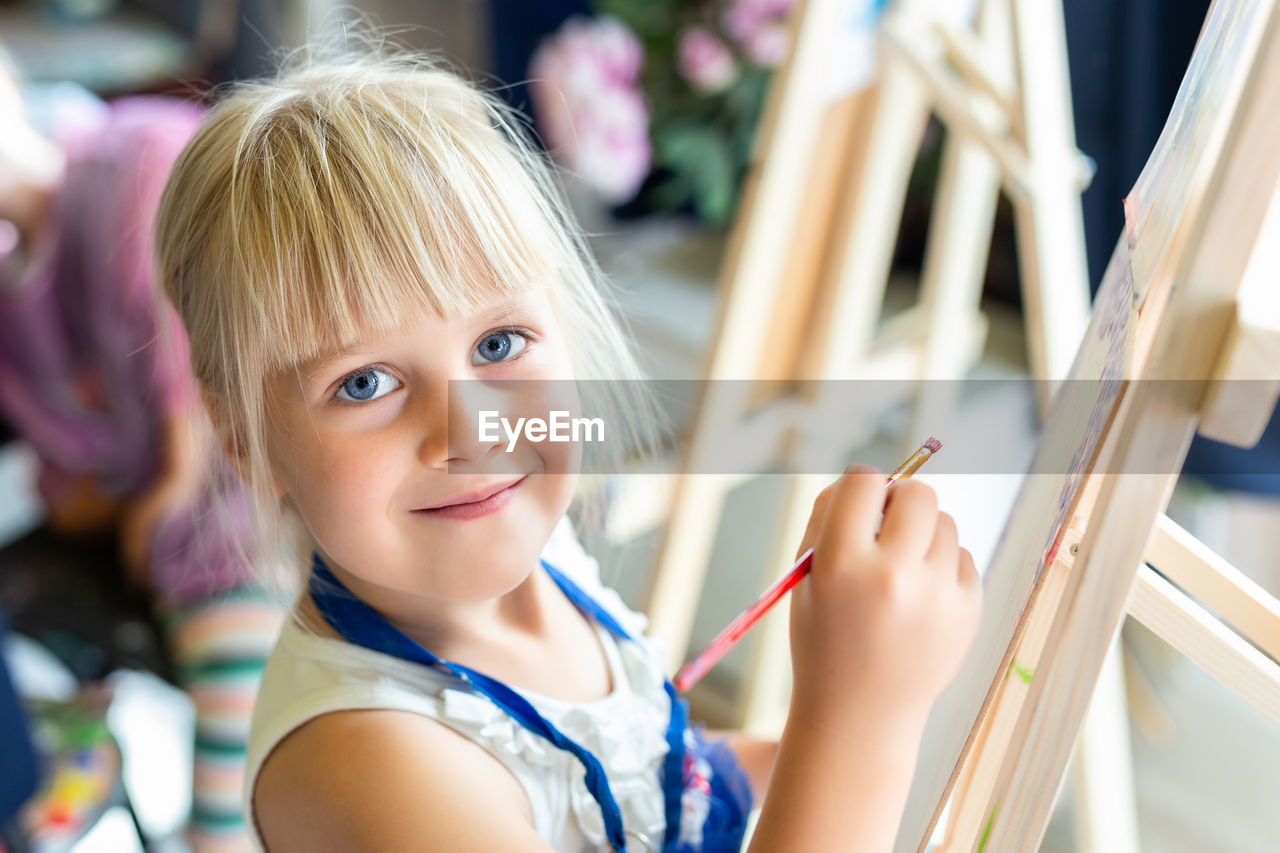 Portrait of smiling girl holding paintbrush indoors