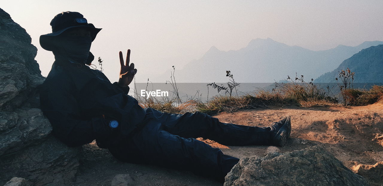 Man showing peace sign while sitting on mountain