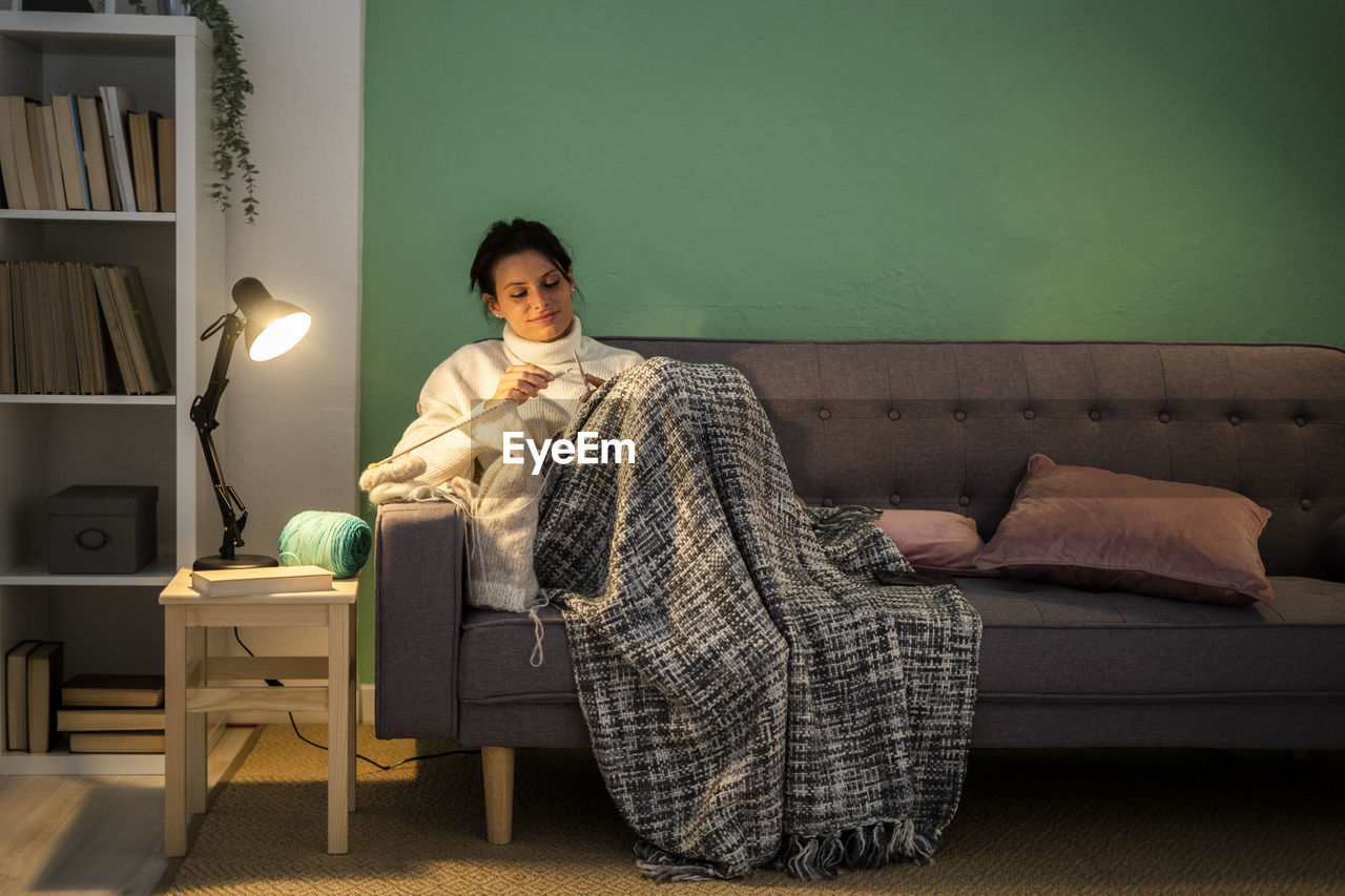 Mid adult woman knitting wool while sitting on sofa at home