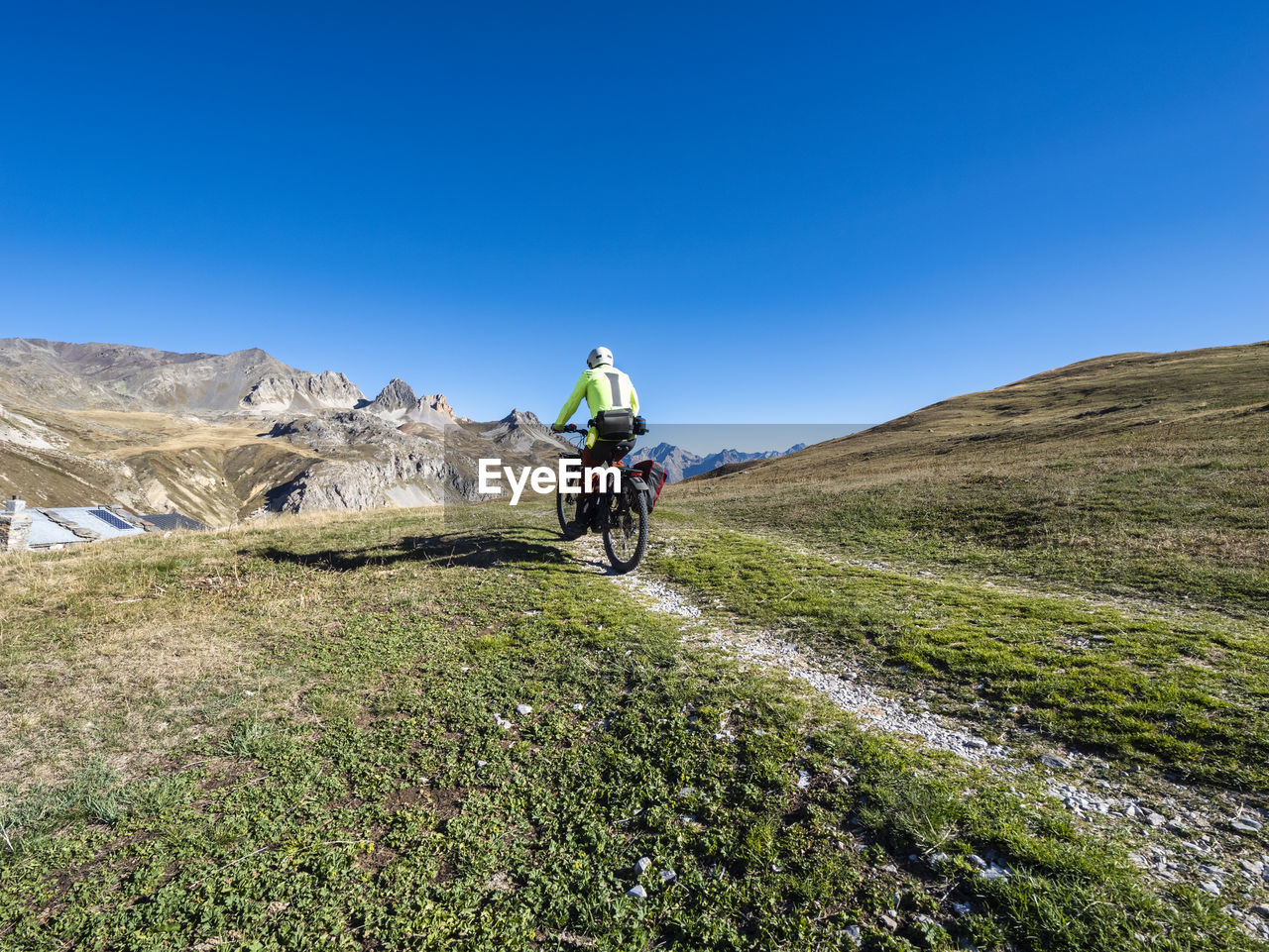 Man riding mountain bike on trail under blue sky, vanoise national park, france