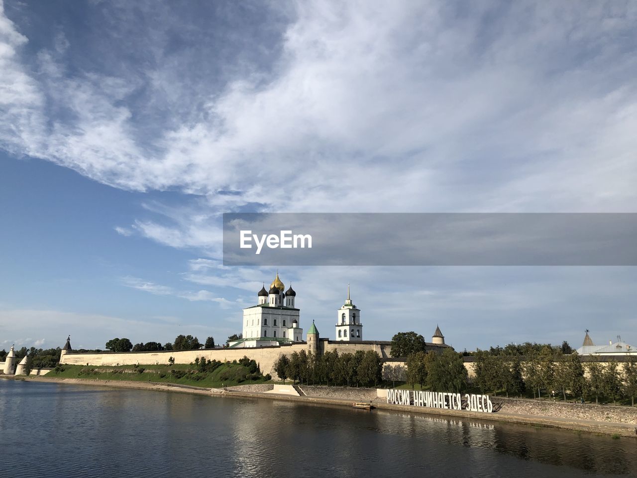 BUILDING BY RIVER AGAINST CLOUDY SKY