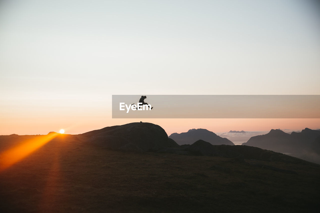 Silhouette of man jumping against mountains during sunset