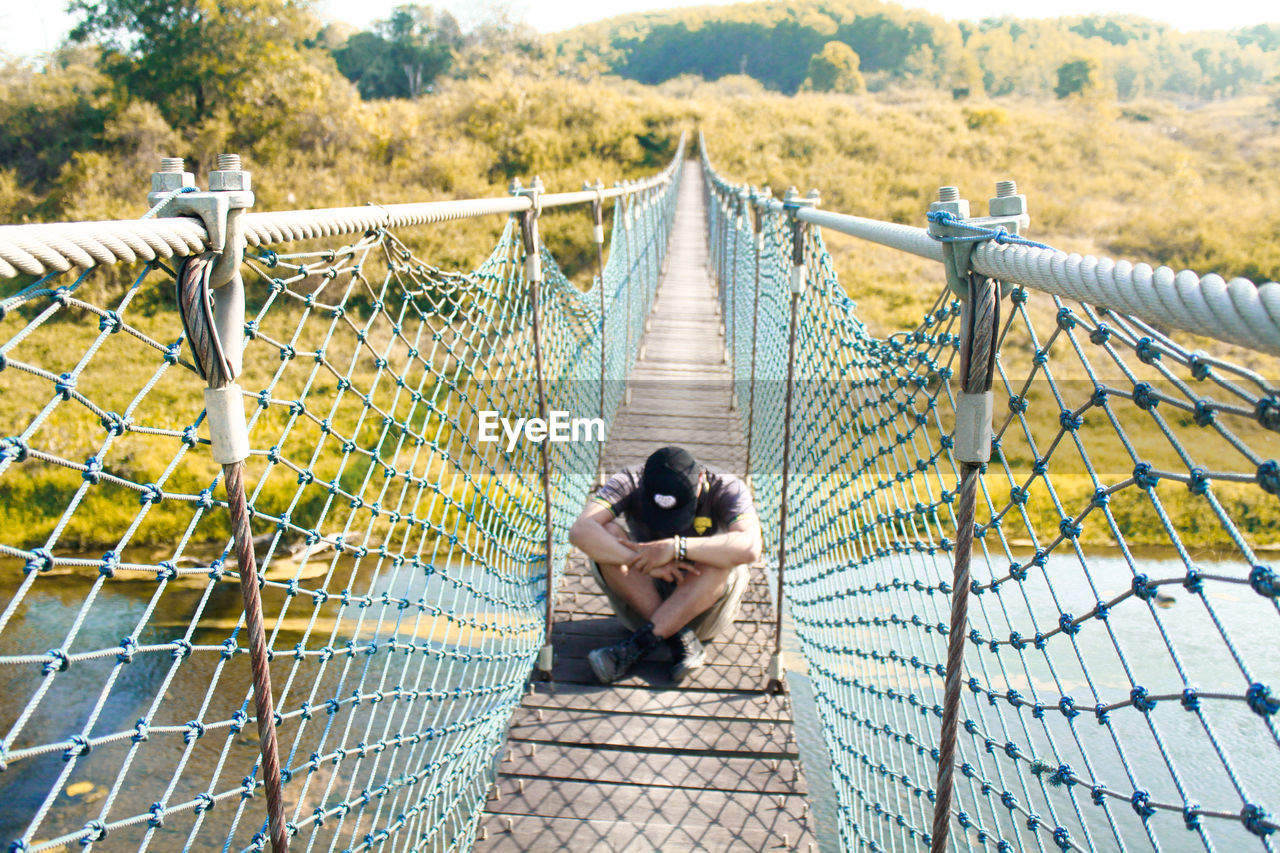 Rear view of man sitting on bridge