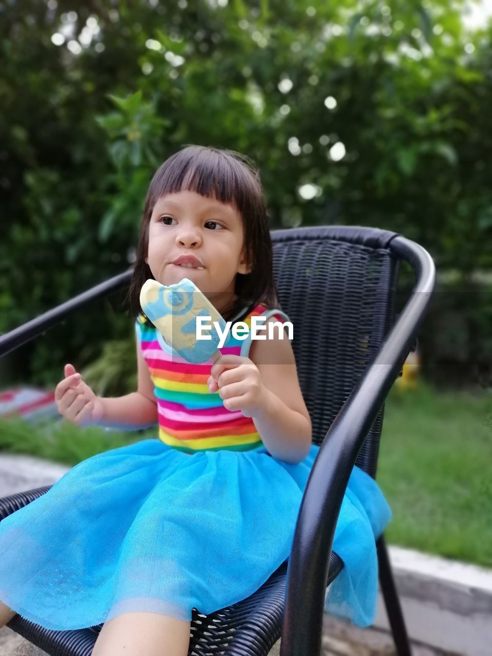 Cute girl eating flavored ice while sitting on chair