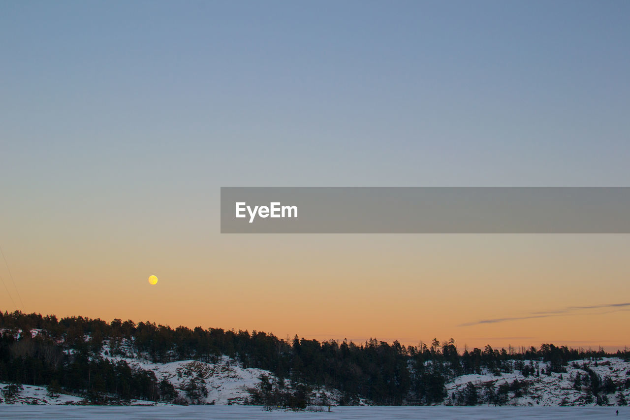 Scenic view of snowy field against clear sky during sunset