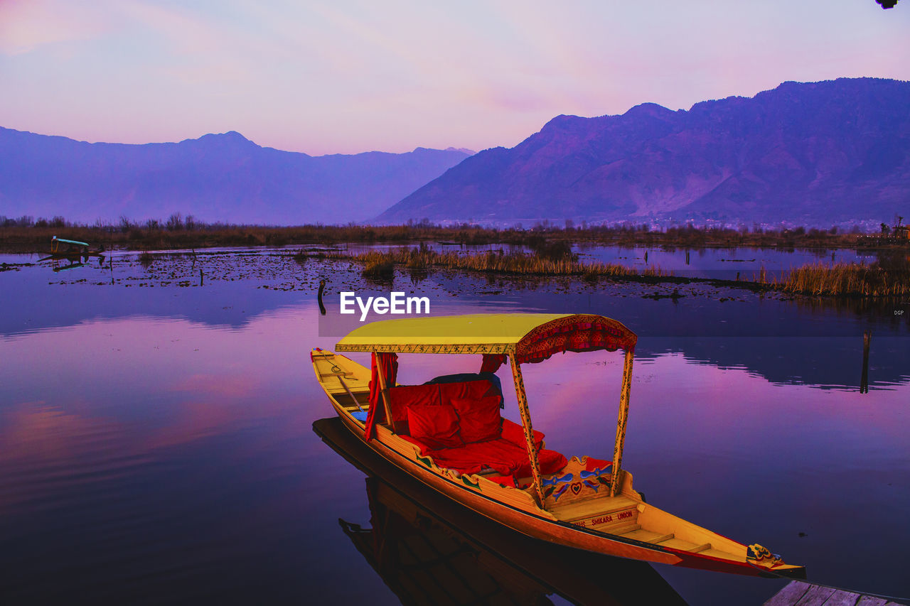 Boat moored by lake against sky during sunset