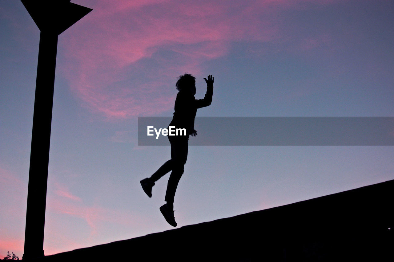 Low angle view of silhouette man jumping against sky during sunset