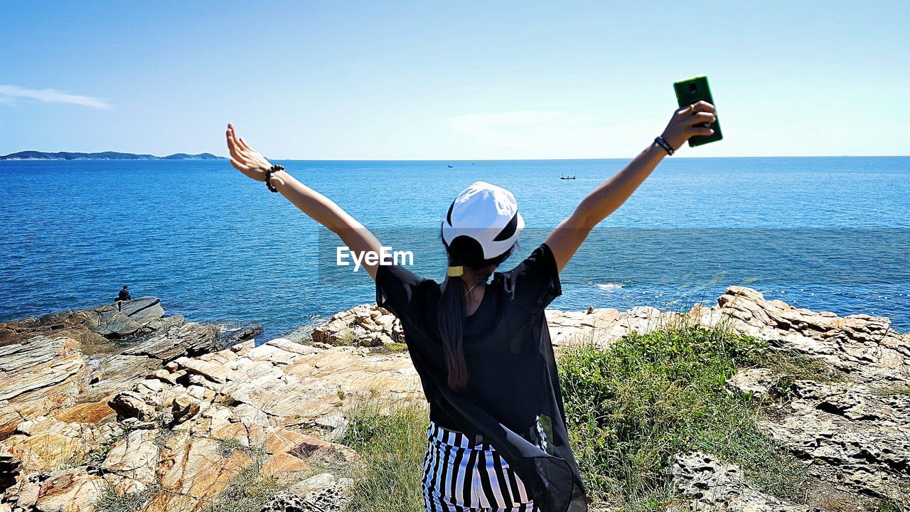 Woman with arms raised looking at sea while standing on cliff