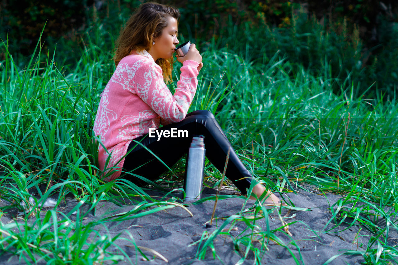 Full length of woman drinking water while sitting on grass