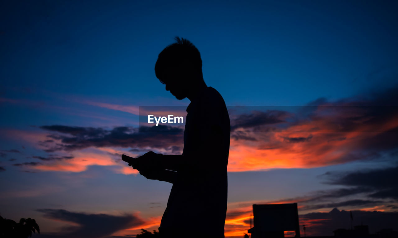 Side view of silhouette man using phone against sky
