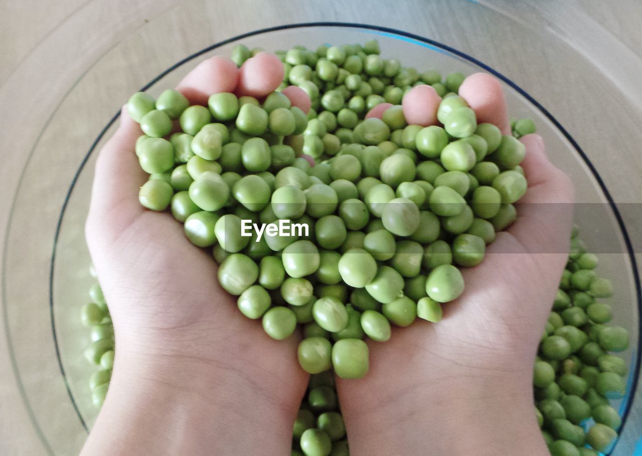 Cropped hands of person holding green peas over bowl