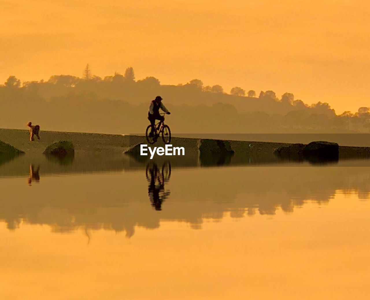 Man riding bicycle at lakeshore against sky during sunset