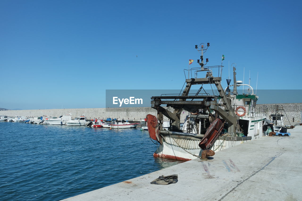 Ship moored at harbor against clear blue sky