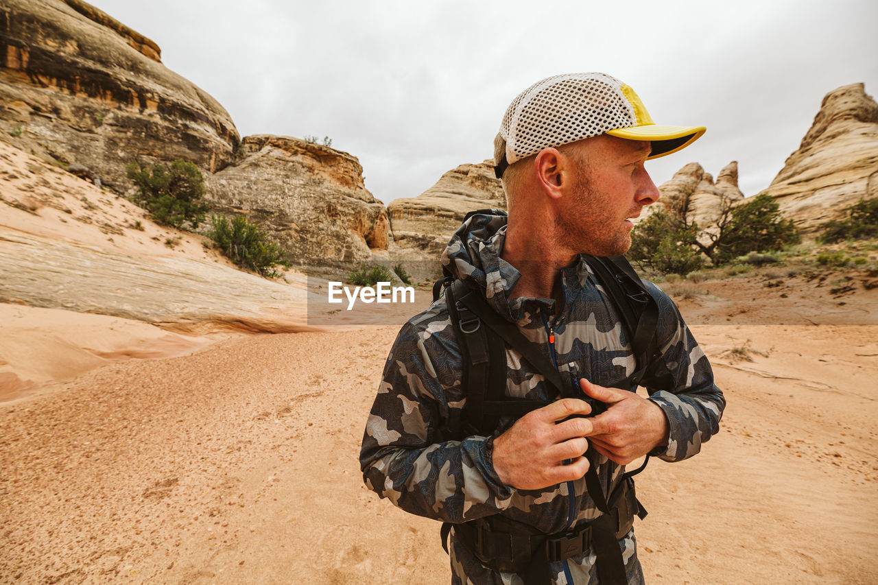 Hiker looks left and buckles his chest strap of backpack in desert