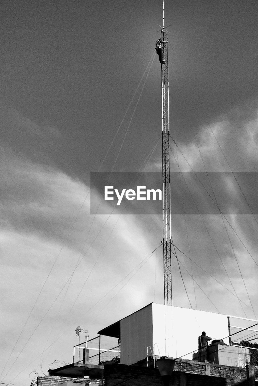 Low angle view of technician working on communications tower against sky