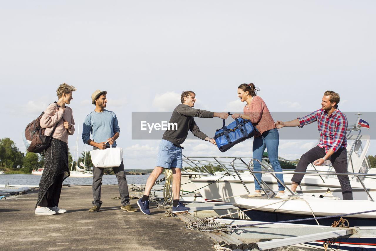 Friends boarding yacht at harbor against sky