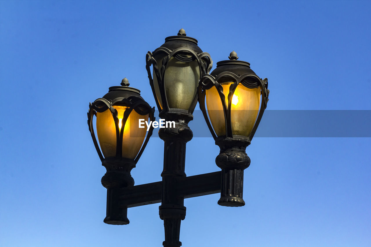 Low angle view of illuminated street light against clear blue sky