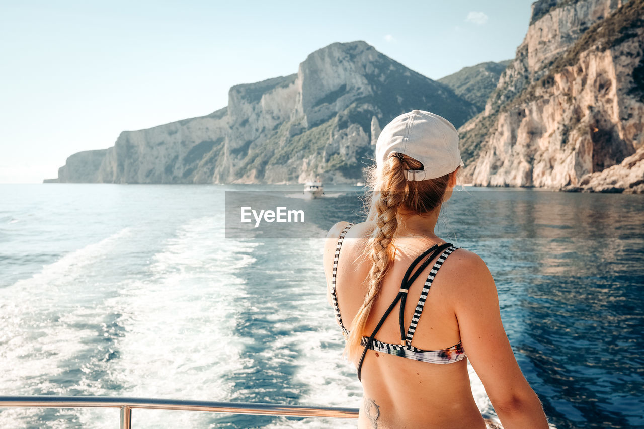 Woman in bikini by sea against mountain