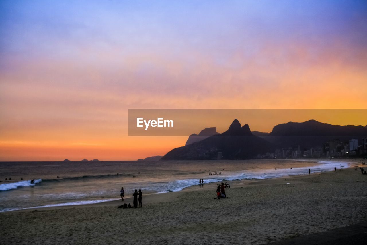 PEOPLE ON BEACH AGAINST SKY DURING SUNSET