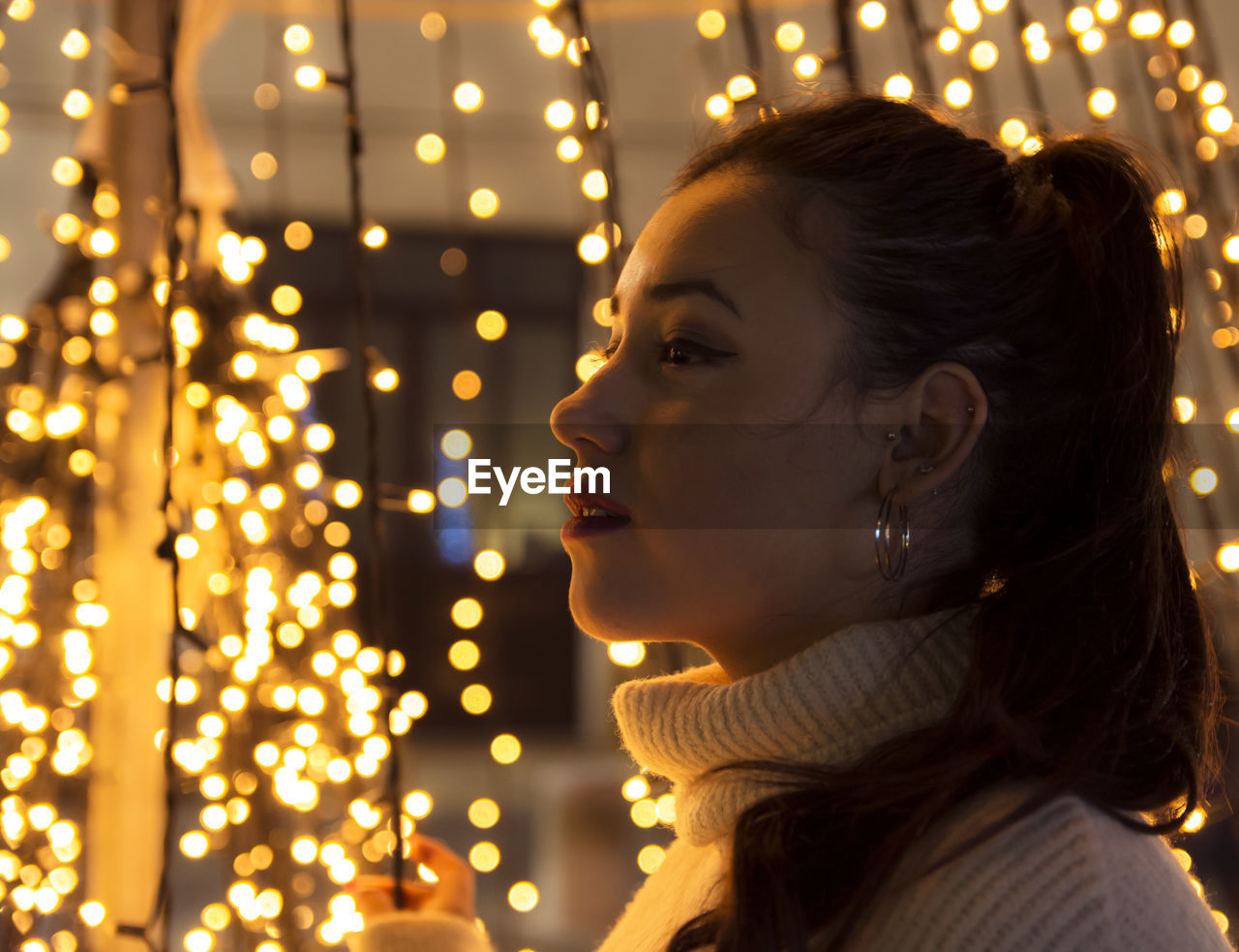 Side view of young woman against illuminated christmas lights
