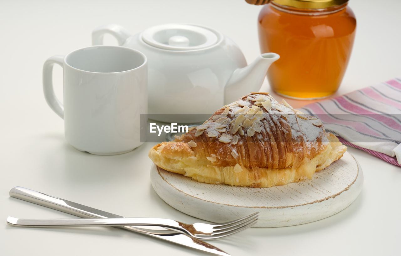 Baked crisp croissant is sprinkled with sugar powder and almond flakes on a wooden board, 